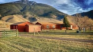 A red barn with a green fence in a rural setting with mountains in the background.