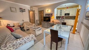 Ein gemütliches Wohnzimmer mit einer Couch, einem Glastisch und einer Küchenzeile mit Schränken und einer Mikrowelle.