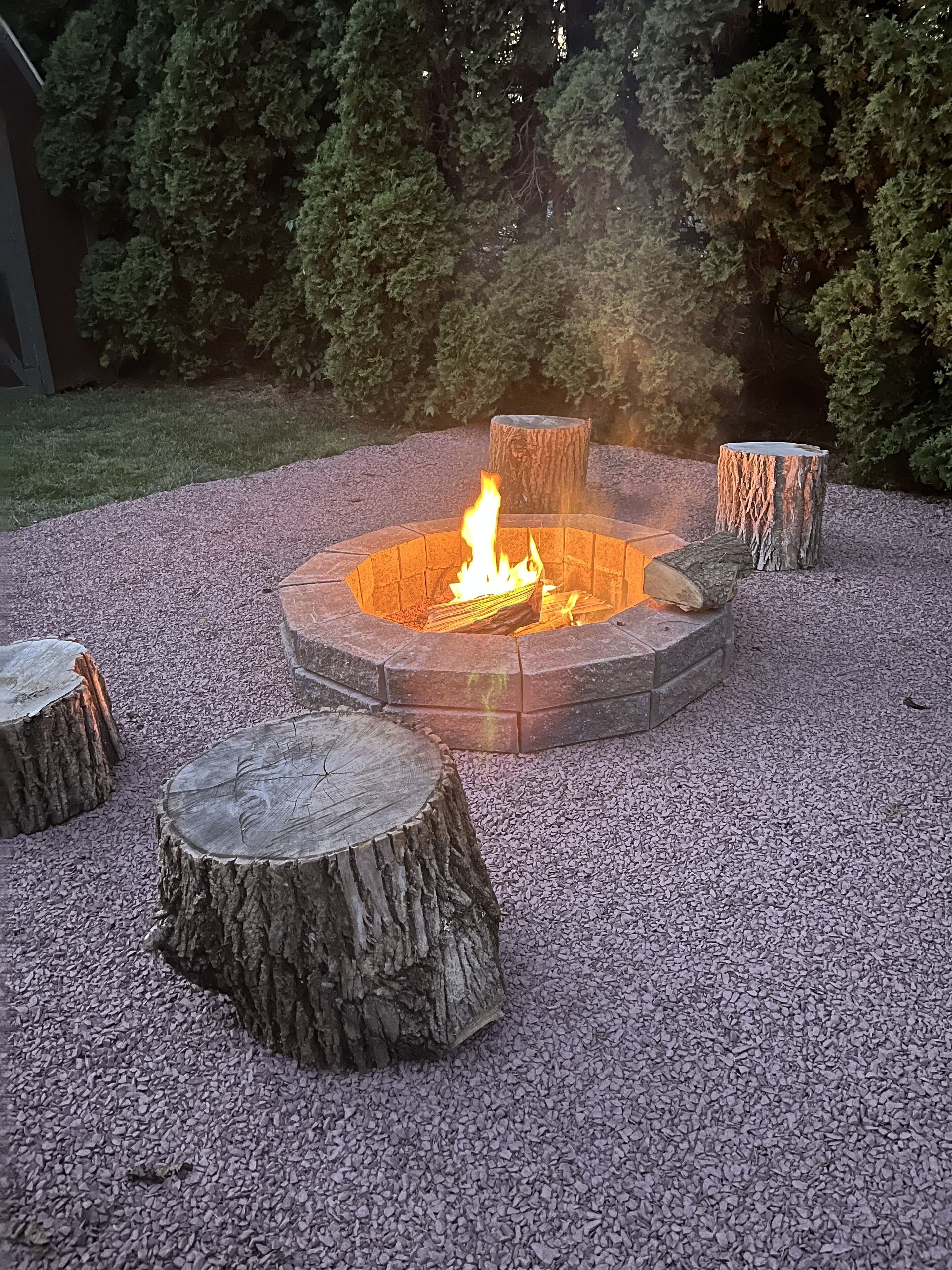 Een ronde vuurkuil met een brandend vuur, omringd door grind en vier zitplaatsen gemaakt van boomstammen.