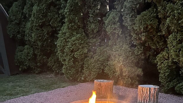 Un pozo de fuego circular con fuego encendido, rodeado de grava y cuatro zonas de asiento hechas con tocones de árbol.