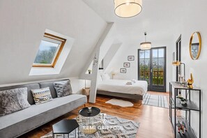 Une chambre de style loft moderne, avec un plafond en pente, un canapé, un lit, une petite table et une console agrémentée d’un miroir.