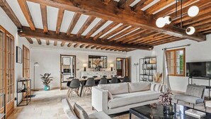 A spacious living area with a high ceiling, wooden beams, a sofa, a coffee table, and a dining area with chairs and a table.