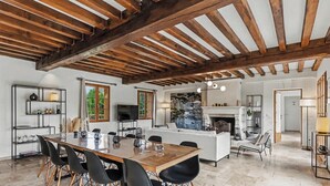 A spacious living area with a wooden ceiling, a dining table with chairs, a sofa, and a fireplace.