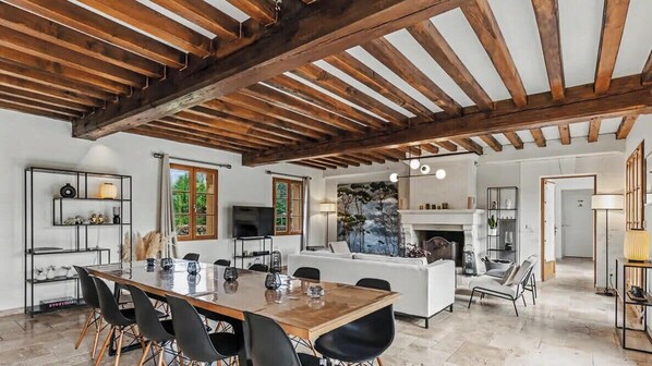 Amplia sala de estar con techo de madera, una mesa de comedor con sillas, un sofá y una chimenea.
