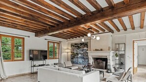 A living room with a fireplace, wooden beams, a TV, and seating.