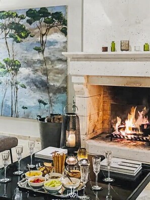 Una mesa de comedor con platos, vasos y una vela, frente a una chimenea con un cuadro en la pared.