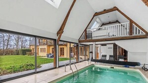 A spacious indoor swimming pool with a glass wall, a second-floor balcony, and a view of a house.