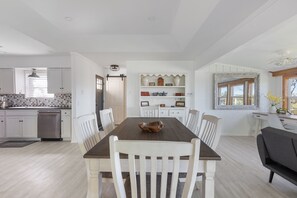 A modern kitchen with white cabinetry, a wooden dining table, and a built-in shelving unit with decorative items.