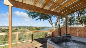Un bain à remous sous une pergola en bois, avec vue sur un lac et des arbres.