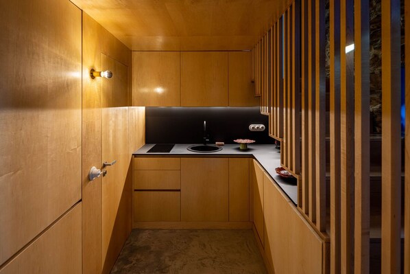 A compact kitchen with wooden cabinetry, a black countertop, and a small sink.