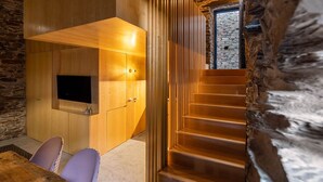 A modern interior with a wooden staircase, a stone wall, and a flat-screen TV mounted on a wooden panel. - Contemporary styled studio (Piódão)