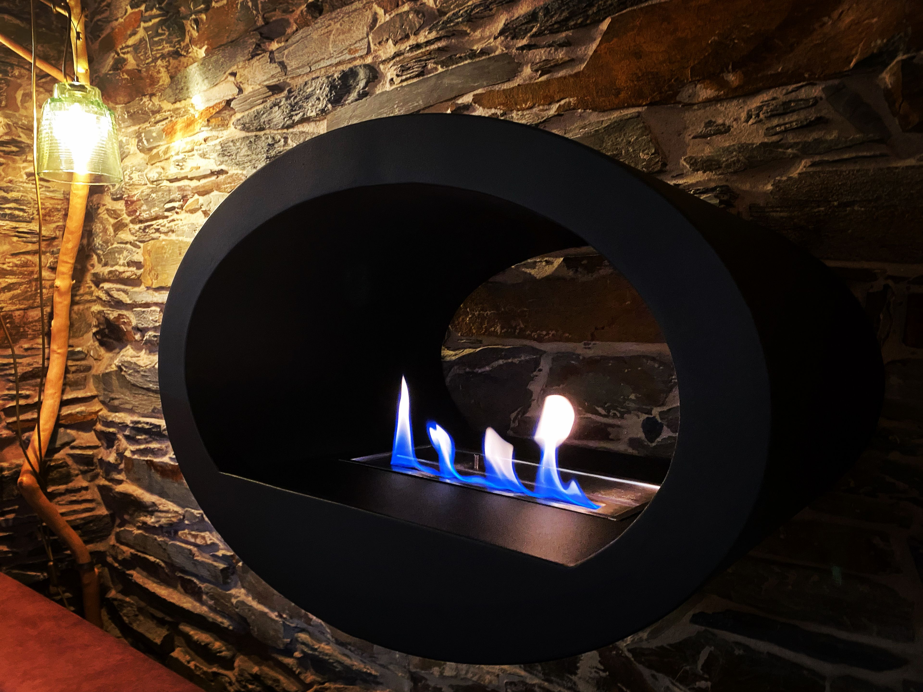 Una chimenea circular con llamas visibles, frente a una pared de piedra.