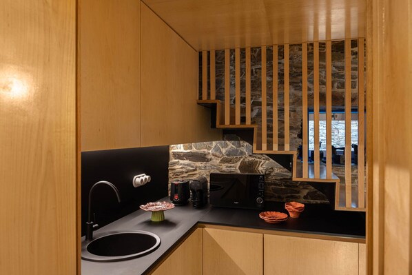 A compact kitchen with a stone backsplash, a coffee machine, and a microwave.