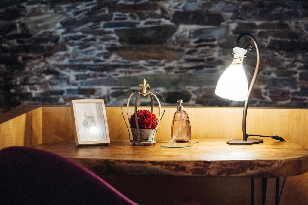 A wooden table with a framed picture, a glass vase with red flowers, and a lamp.