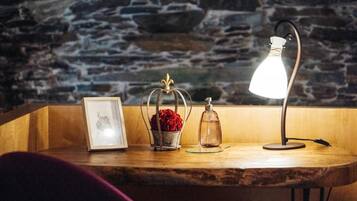 A wooden table with a framed picture, a glass vase with red flowers, and a lamp.