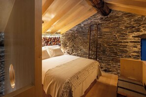 A bedroom with a stone wall, a wooden ceiling, and a bed with a white bedspread. - Contemporary styled studio (Piódão)