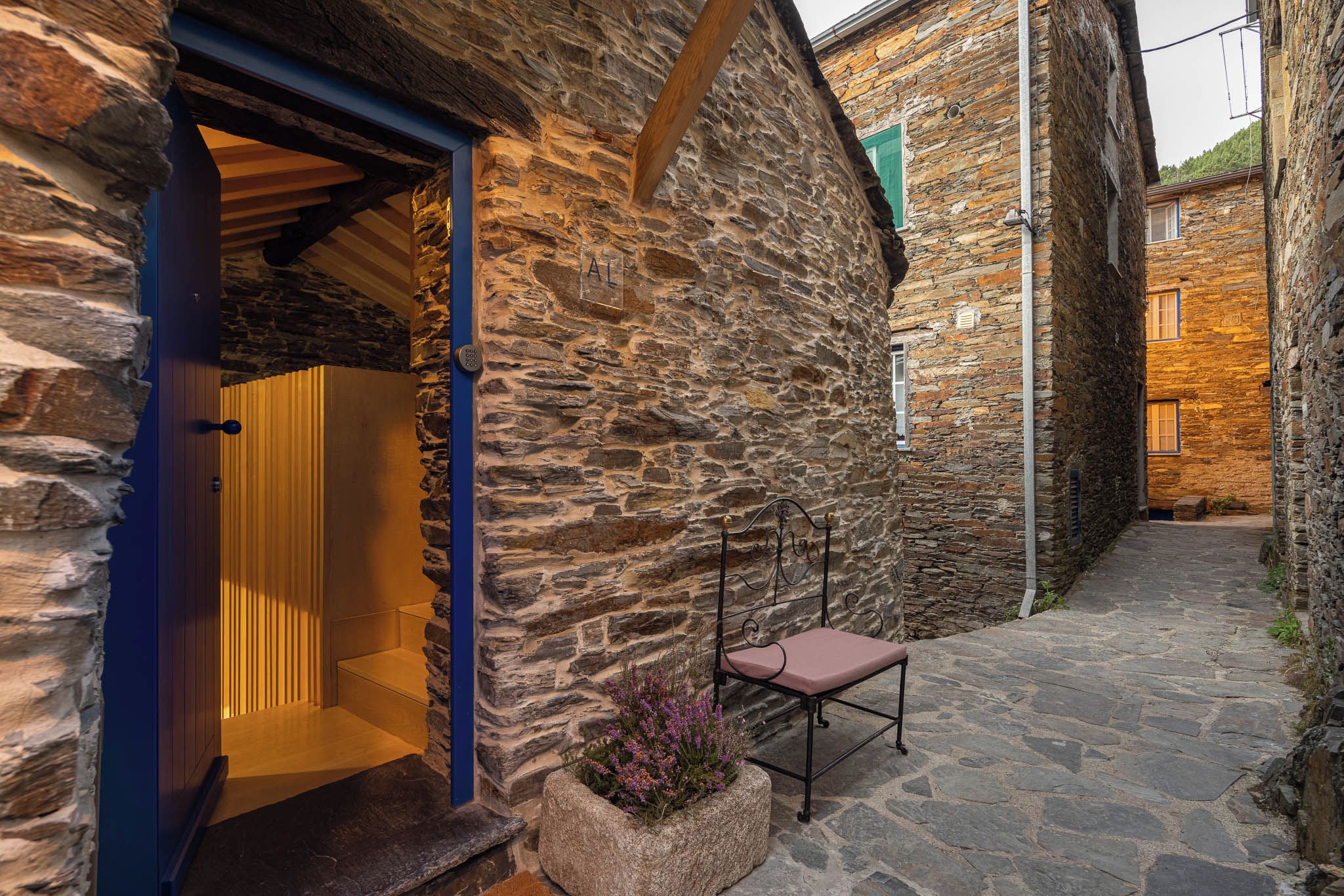 A stone building with a wooden door, a bench, and a stone pathway.