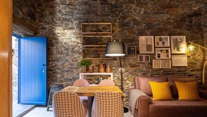 A cozy room with a stone wall, a blue door, a wooden table, a sofa with yellow pillows, and framed pictures on the wall. - Contemporary styled studio (Piódão)