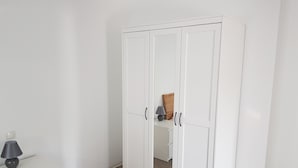 Un armario blanco con puertas de espejo y una mesita con lámpara.