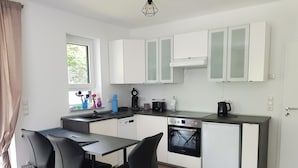 Una cocina moderna con armarios blancos, horno empotrado, cafetera y un comedor con sillas negras.