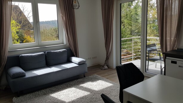 Una sala de estar moderna con un sofá gris, una mesa blanca y vistas a un balcón con barandilla.