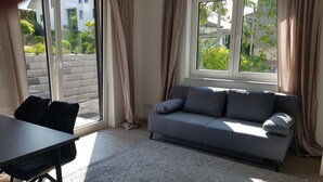 Una sala moderna con un sofá gris, una mesita y un ventanal con cortinas.