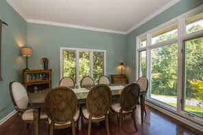 A dining room with a table set for six, surrounded by chairs, large windows, and a lamp on the wall.