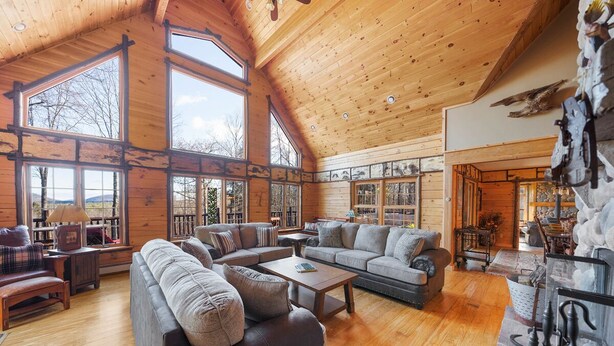 A spacious living room with a high ceiling and large windows, furnished with sofas and a coffee table. - Private Lincoln Log Luxury Lodge in the Adirondacks  (Johnsburg)