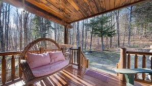 A wooden deck with a wicker swing chair and a bench, overlooking a forested area. - Private Lincoln Log Luxury Lodge in the Adirondacks  (Johnsburg)