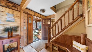 A wooden cabin interior with a wooden staircase, a bench with a 'welcome' pillow, and a door leading to an outdoor area. - Private Lincoln Log Luxury Lodge in the Adirondacks  (Johnsburg)