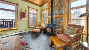 A cozy room with a stone fireplace, wooden furniture, and large windows. - Private Lincoln Log Luxury Lodge in the Adirondacks  (Johnsburg)