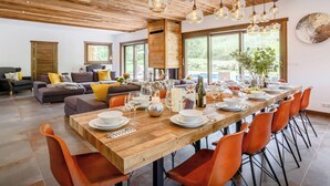 A spacious dining area with a long wooden table set for a meal, surrounded by orange chairs. - Chalet Woodman - alpine base for 14, spa and summer pool - OVO Network (Saint-Gervais-les-Bains)