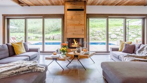 A modern living room with a fireplace, large windows, and a view of a swimming pool. - Chalet Woodman - alpine base for 14, spa and summer pool - OVO Network (Saint-Gervais-les-Bains)