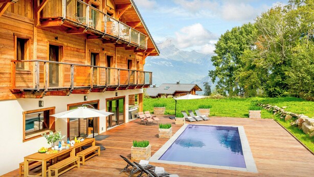 A wooden chalet with a balcony, a pool, and a dining area with outdoor furniture. - Chalet Woodman - alpine base for 14, spa and summer pool - OVO Network (Saint-Gervais-les-Bains)