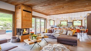 A modern living room with a fireplace, large windows, and a dining area. - Chalet Woodman - alpine base for 14, spa and summer pool - OVO Network (Saint-Gervais-les-Bains)