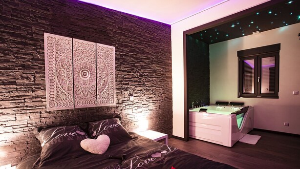 A modern bedroom with a stone wall, a bed with a heart-themed bedspread, a bedside table, and a nightstand. - LE CHALET ZEN LOVE (Foucherans)