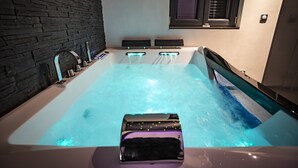 A modern bathroom with a large bathtub, a black stone wall, and a window with blinds. - LE CHALET ZEN LOVE (Foucherans)