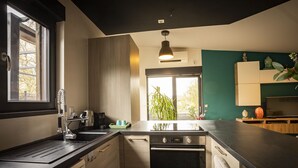 A modern kitchen with a built-in oven, a sink, and a window overlooking a garden. - LE CHALET ZEN LOVE (Foucherans)