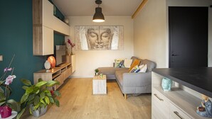 A modern living space with a sofa, coffee table, and decorative items. There is a television on a wooden stand, a wall-mounted shelf, and a door in the background. - LE CHALET ZEN LOVE (Foucherans)