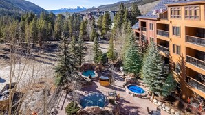 A resort with multiple swimming pools, a mountain backdrop, and a forested area. - Spacious Top-Floor 3-bed Springs Condo: 5 minute walk to gondola and restaurants (Keystone)