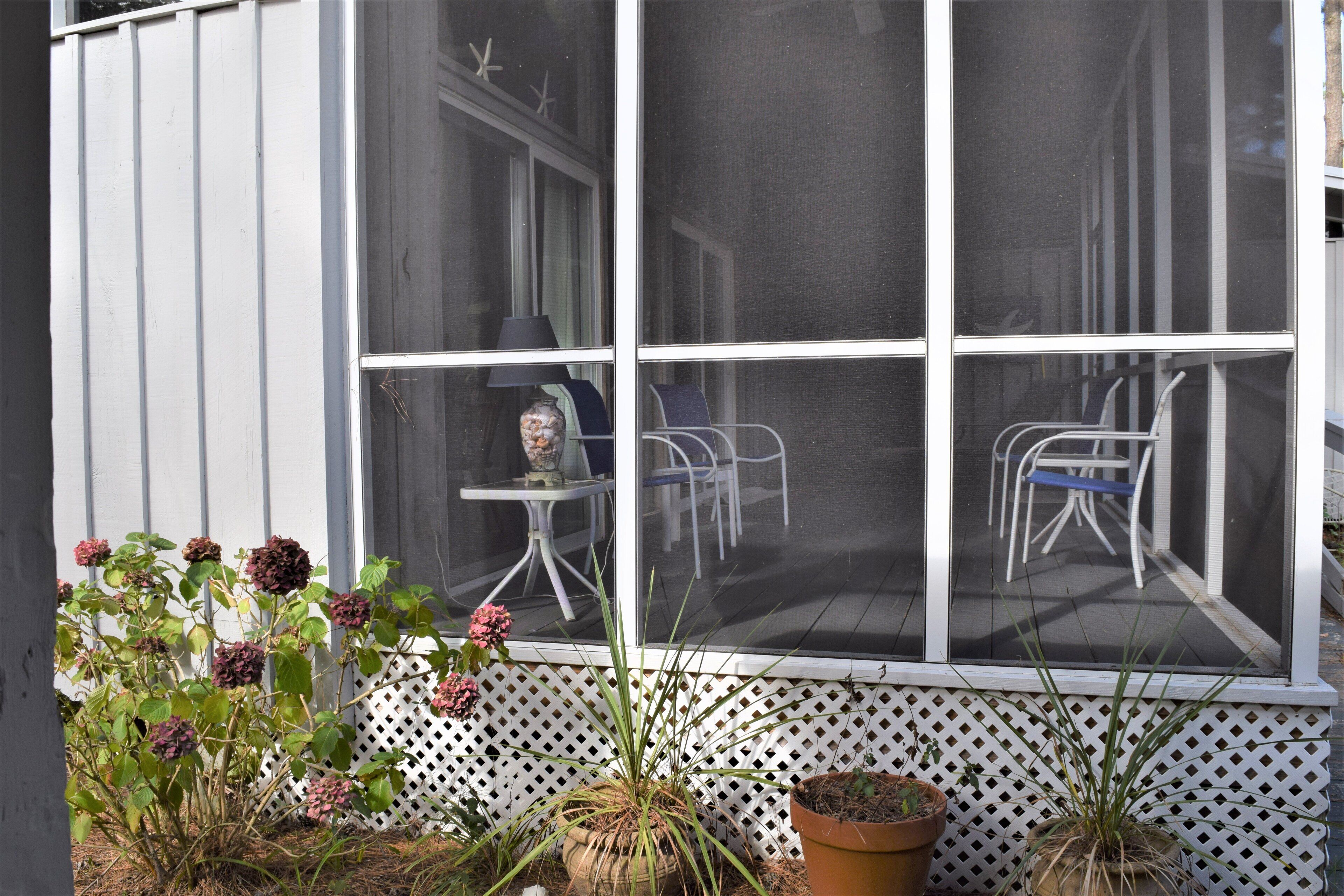 A screened porch with a white picket fence, a table, and chairs.