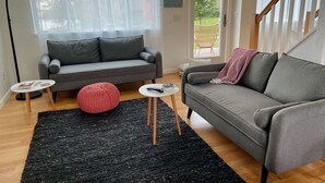 A modern living room with a grey sofa, a red pouf, and a black rug. - Peaceful River Retreat with Fireplace & Panoramic Views (Cementon)