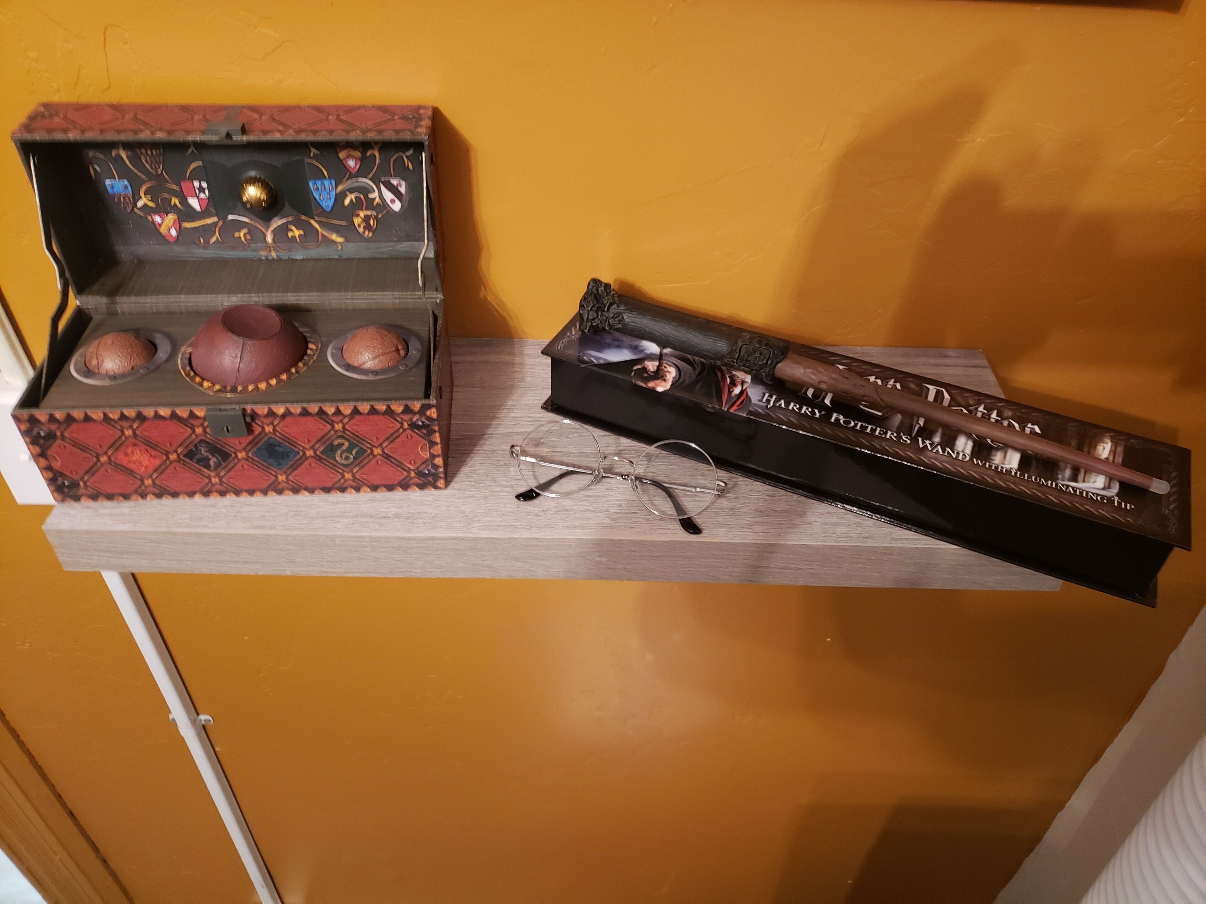 A wooden shelf with a decorative box containing three brown objects and a Harry Potter-themed wand.