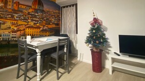 Un comedor con una mesa y sillas, un pequeño árbol de Navidad y un televisor sobre un mueble.