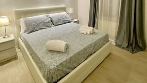 Un dormitorio moderno con una cama grande, una mesita de noche con lámpara y una ventana con cortinas.