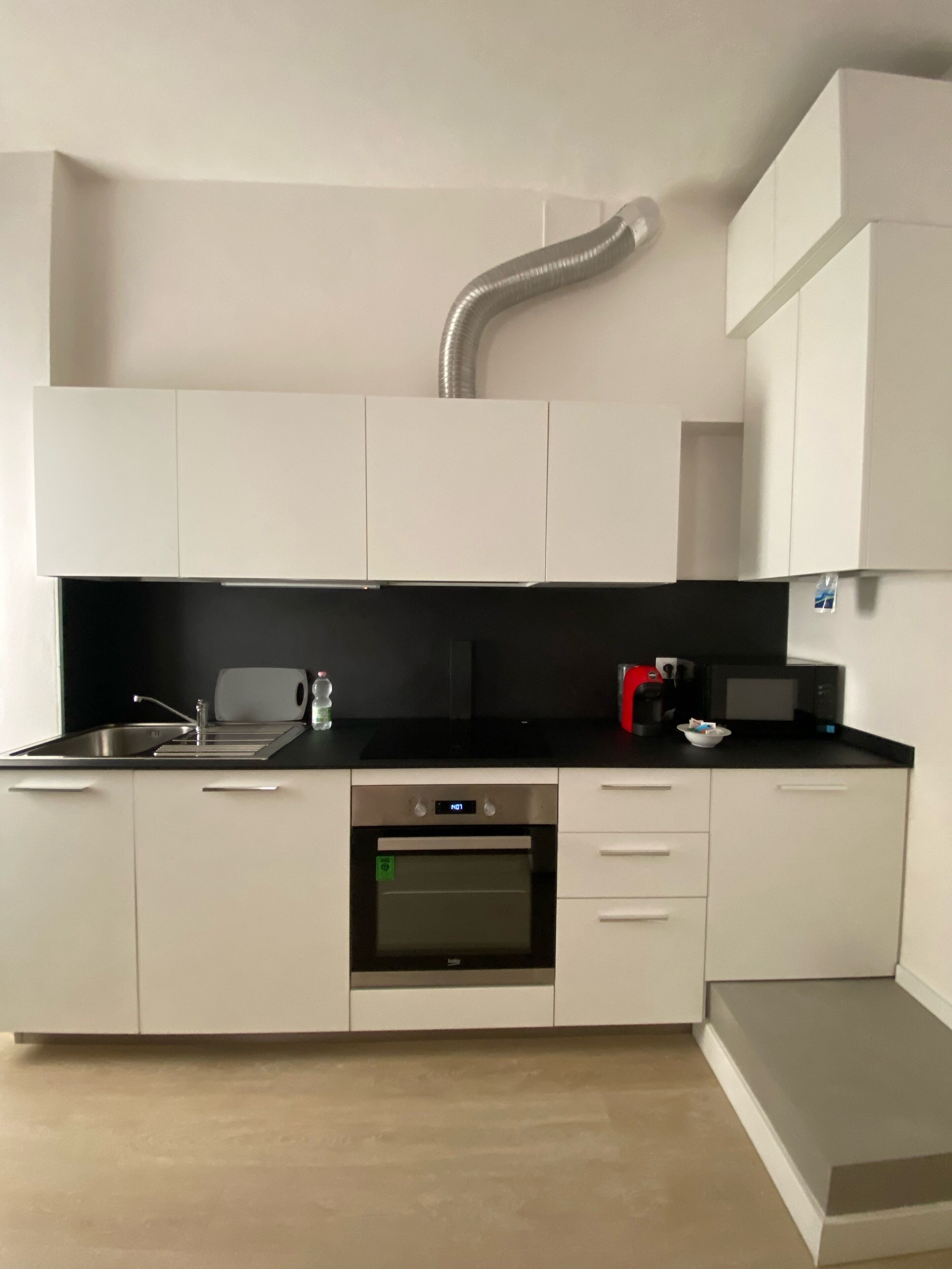 Eine moderne Küche mit weißen Schränken, einer schwarzen Arbeitsplatte, einer Edelstahl-Spüle, einer Mikrowelle und einem Backofen.
