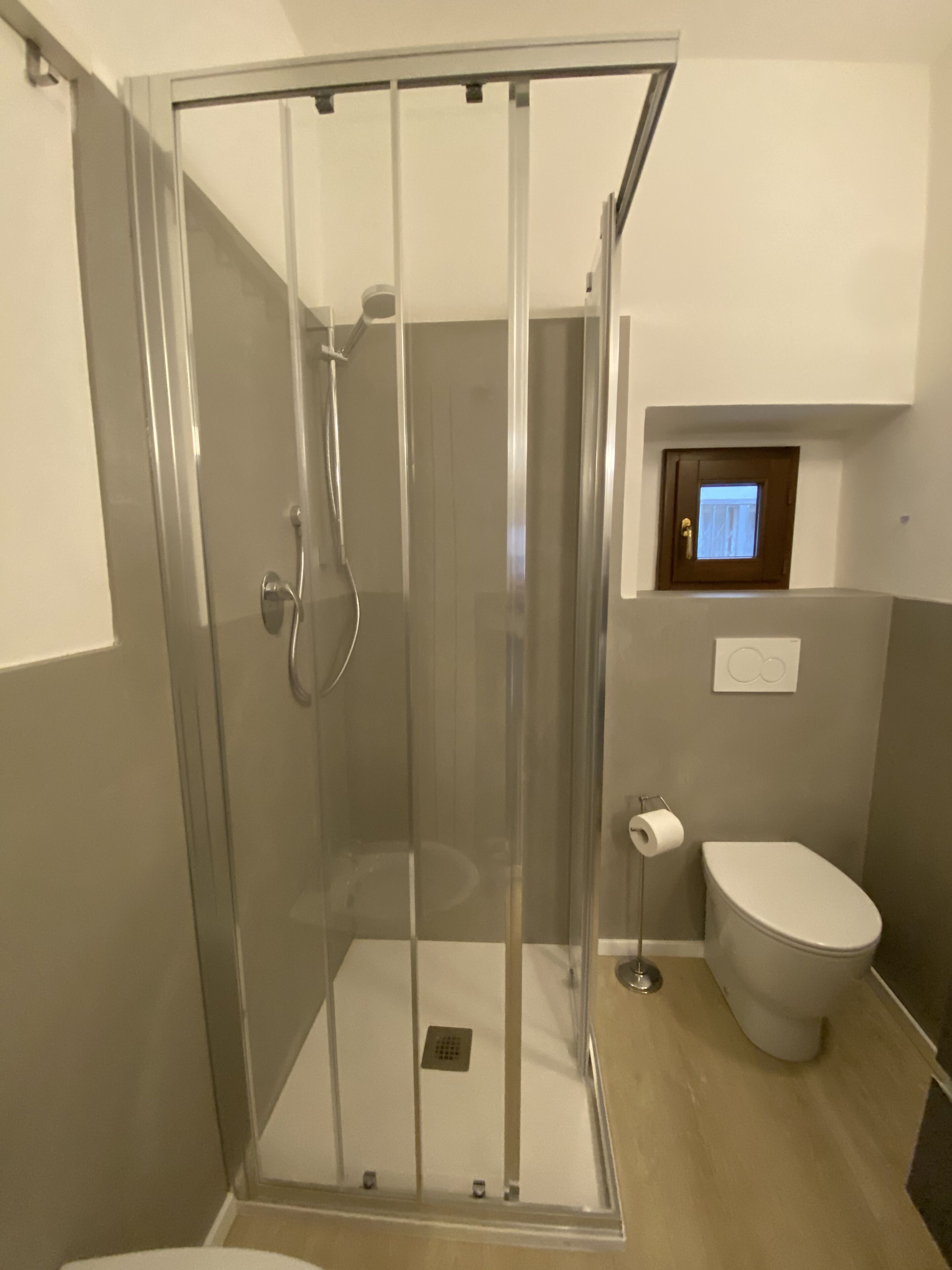 Un baño moderno con ducha de vidrio, inodoro y una pequeña ventana sobre el inodoro.