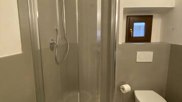 Un baño moderno con ducha de vidrio, inodoro y una pequeña ventana sobre el inodoro.