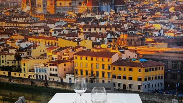 Una mesa de comedor dispuesta con platos, vasos y velas, con un mural de un paisaje urbano de fondo.