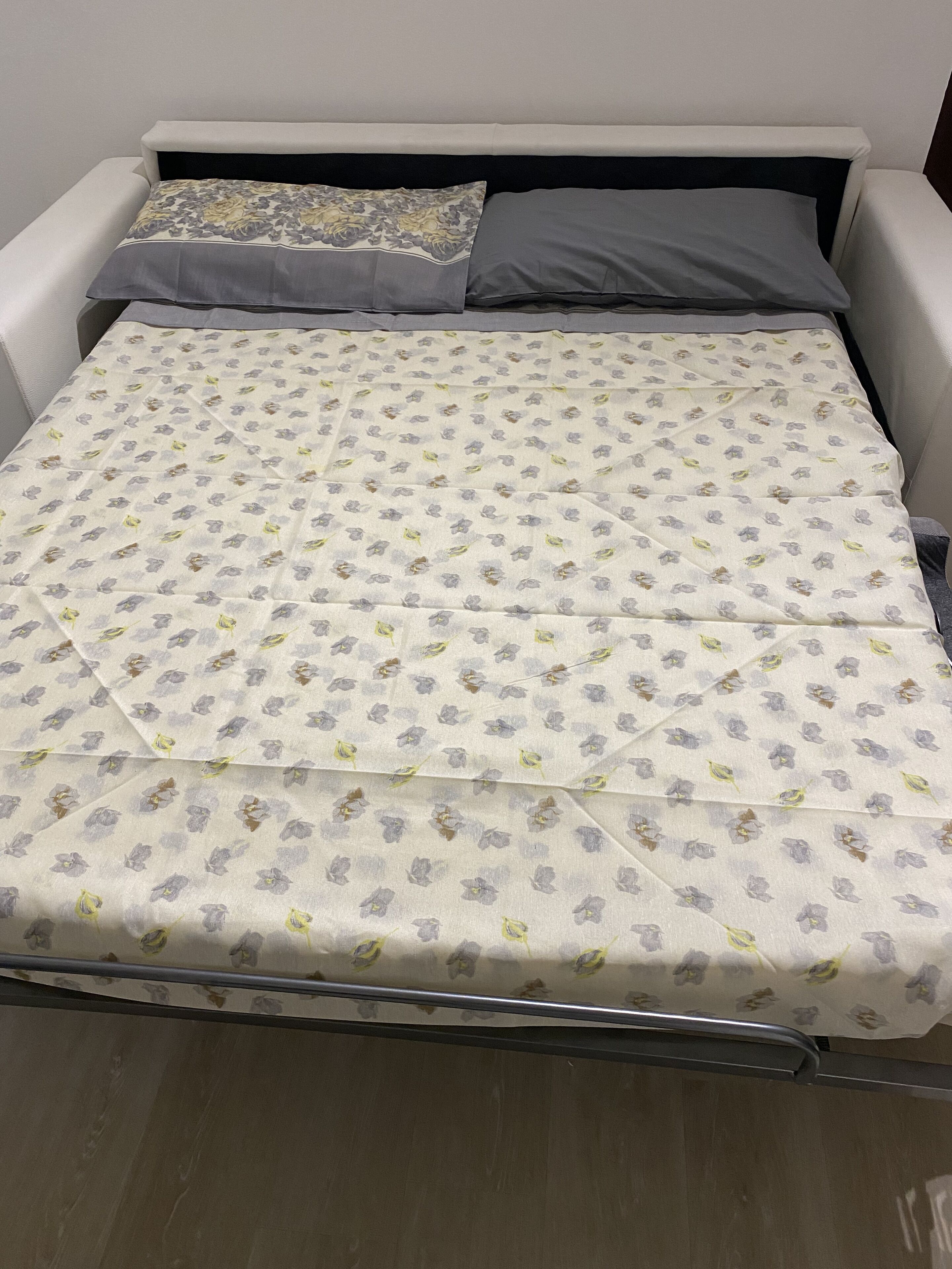 A bed with a floral-patterned bedspread, two pillows, and a metal frame.